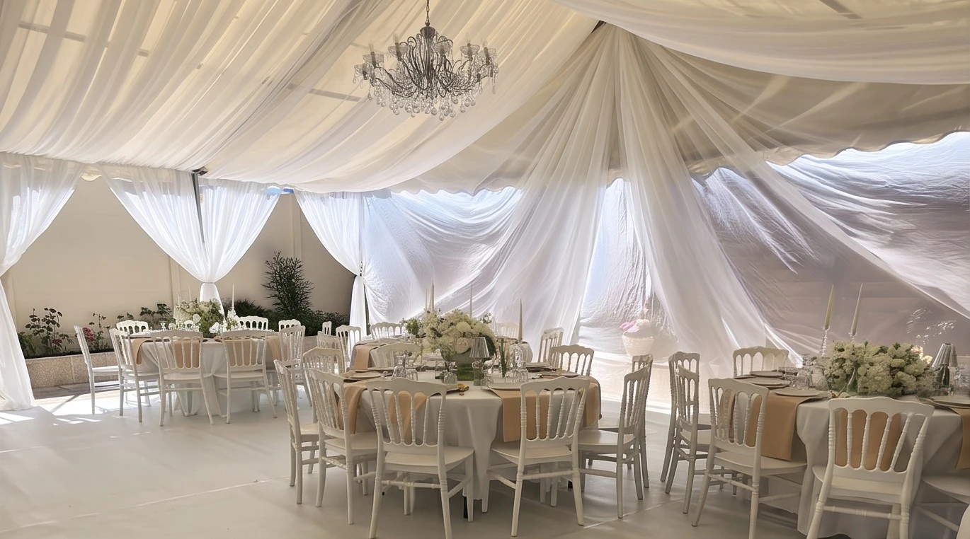 Chapiteau de réception décoré avec voilage blanc, éclairage chaud et tables dressées pour un événement